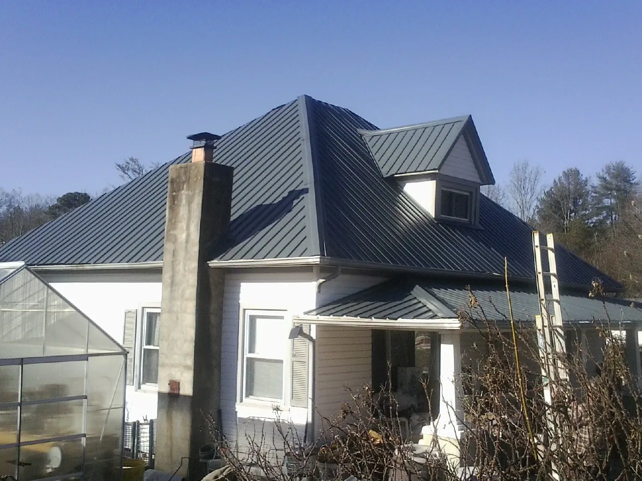 Dark blue standing seam metal roof on a white farmhouse with dormer — Slate & Tile Roof Repair by Roofing Brothers in Calmar