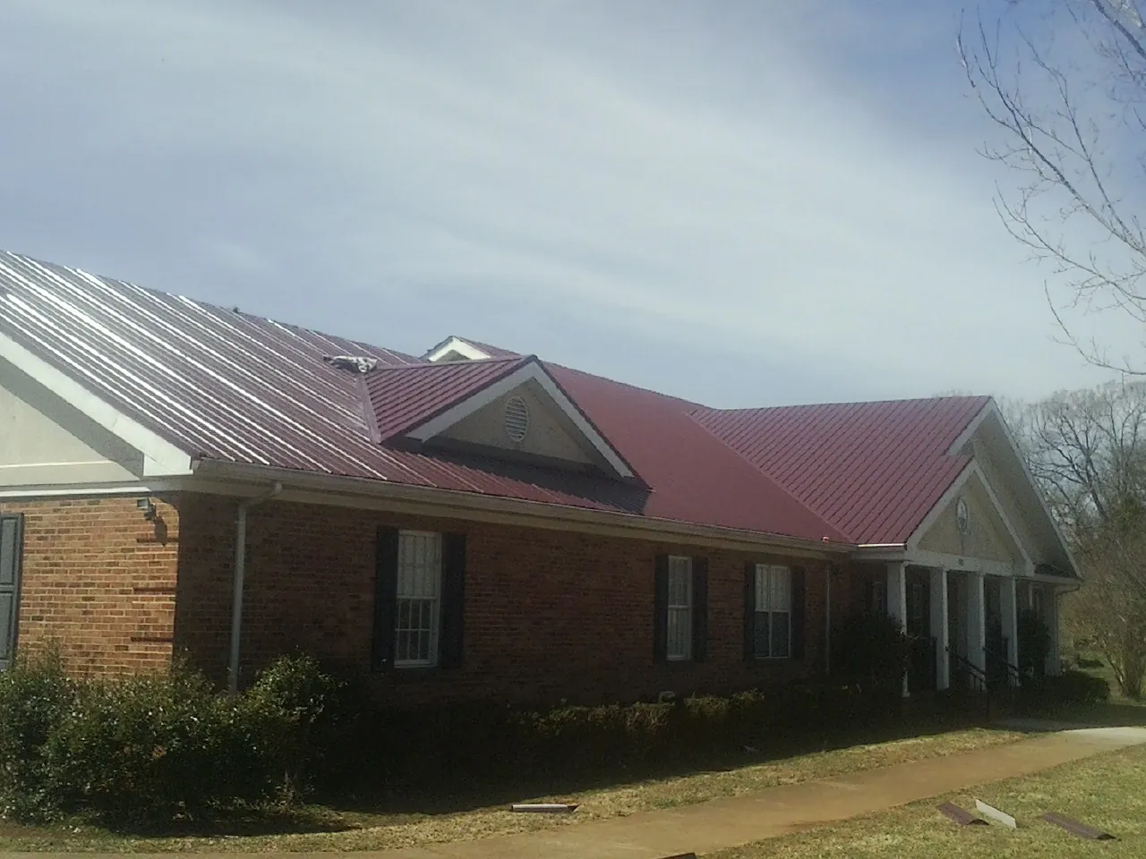 Red metal roof with gabled entries on a long brick building, from a Hail Damage Roof Repair job in Calmar