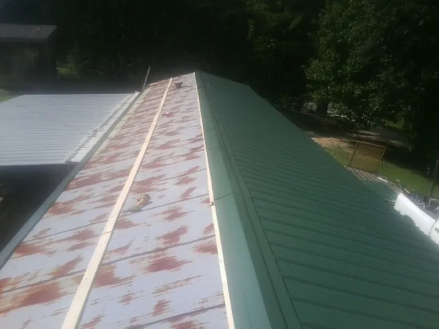 Old rusted panels beside newly installed green metal roofing — Wind Damage Roof Repair by Roofing Brothers in Calmar