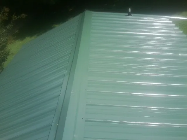 New green metal panels meeting at the ridge of a roof — Flat Roof Repair work by our crew in Calmar