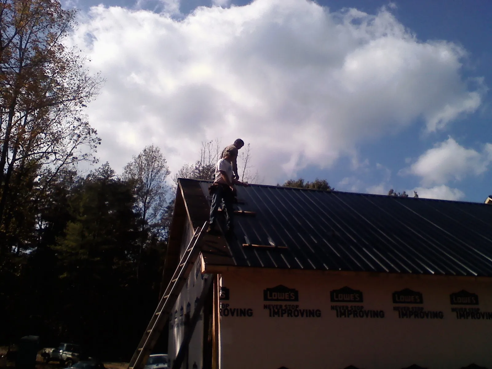 Roofer fastening dark metal panels high against a cloudy sky, from a Roof Inspection job in Calmar
