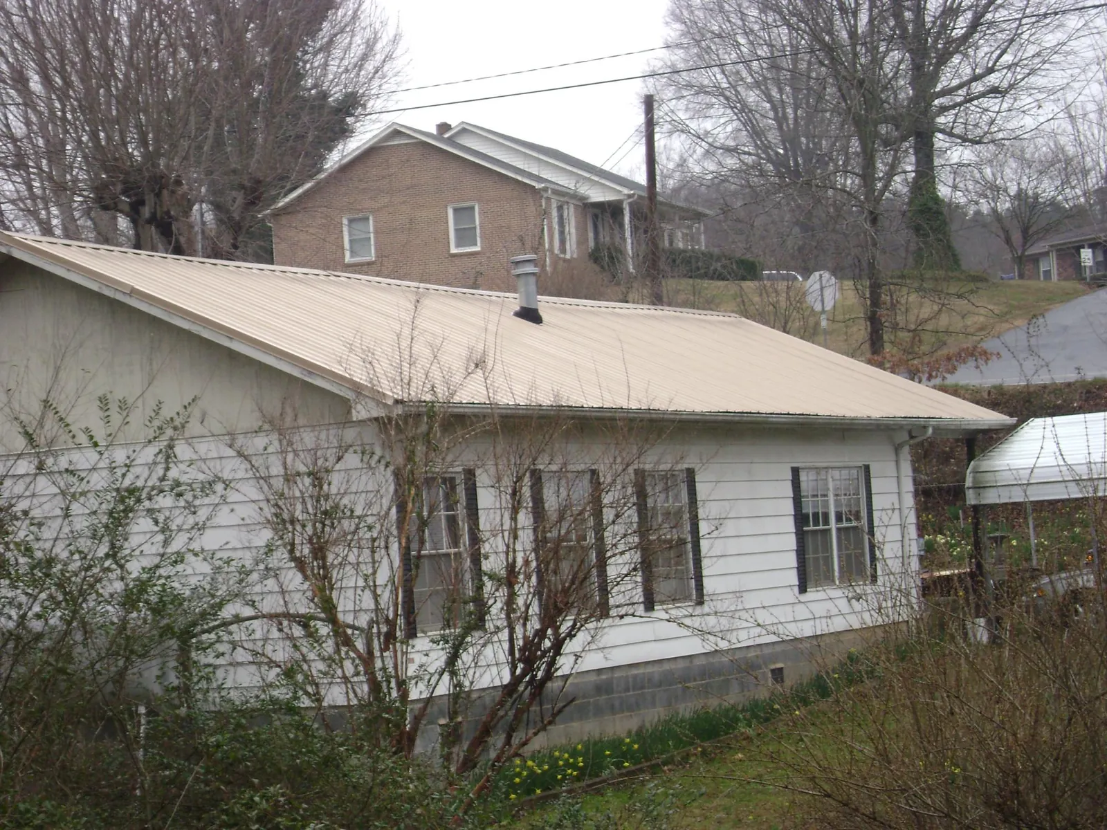 Tan metal roof on a white sided house set into a hillside — Commercial Roofing by Roofing Brothers in Calmar