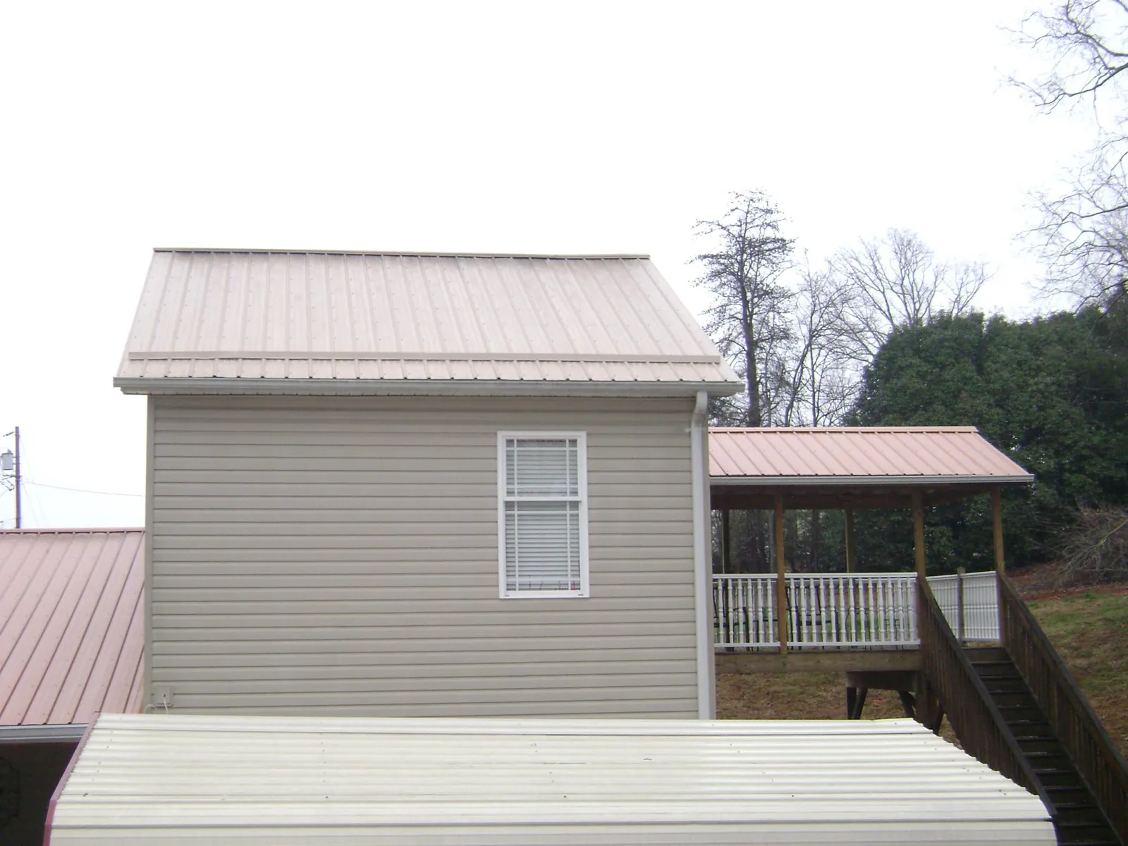 Tan metal roofs on a two story addition and attached porch, from a Roof Replacement job in Calmar